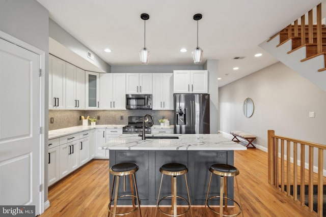 kitchen featuring white cabinetry, appliances with stainless steel finishes, a center island with sink, and light stone counters