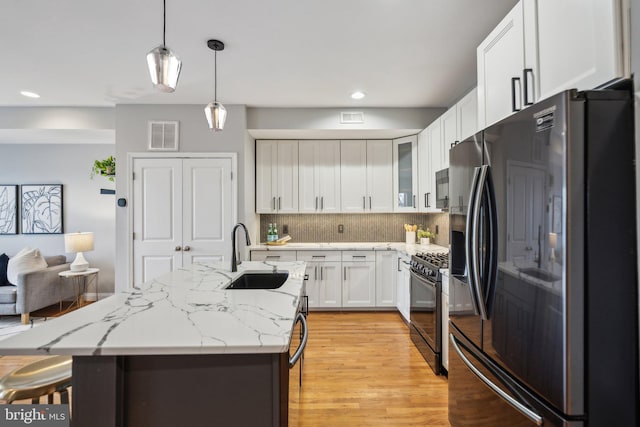 kitchen featuring pendant lighting, sink, stainless steel fridge, white cabinets, and black range with gas stovetop