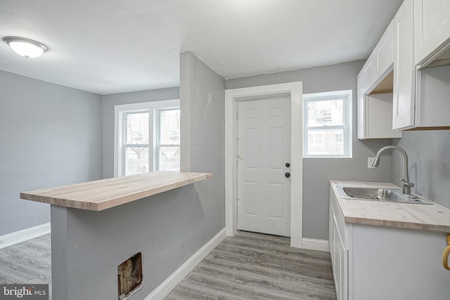 kitchen with white cabinetry, sink, light hardwood / wood-style floors, and kitchen peninsula