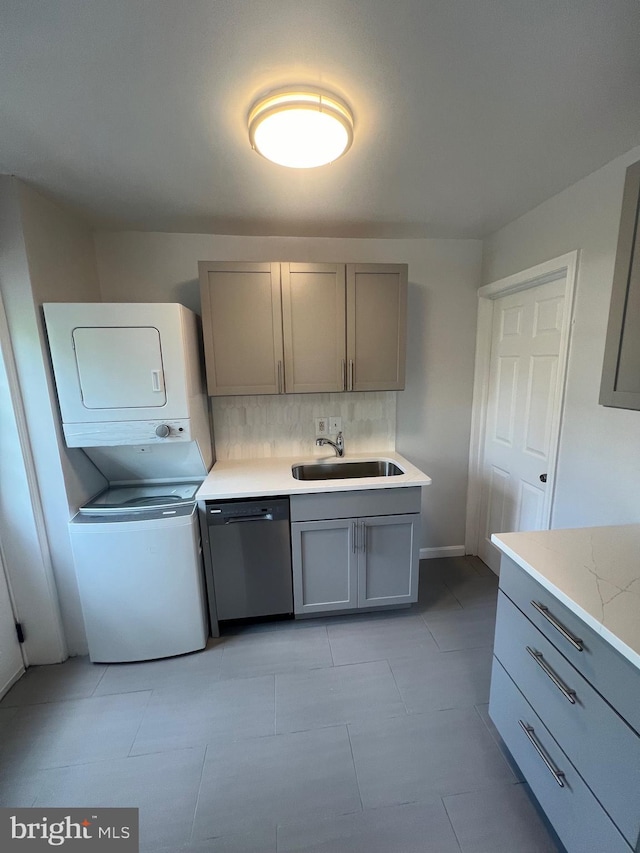 kitchen with stacked washer / drying machine, sink, gray cabinetry, dishwasher, and decorative backsplash