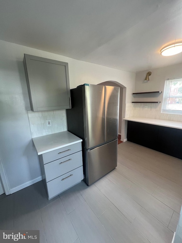 kitchen with gray cabinetry, backsplash, and stainless steel refrigerator