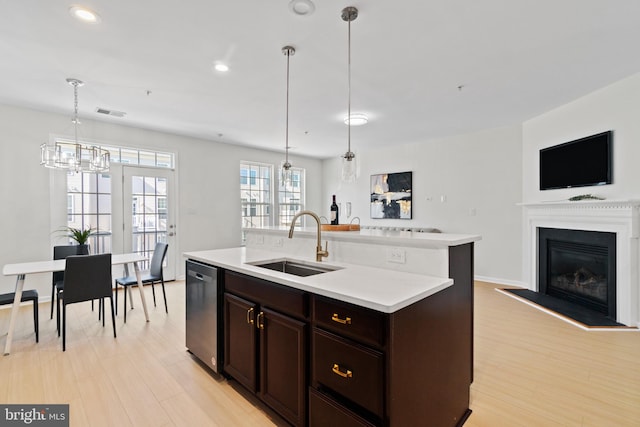 kitchen with stainless steel dishwasher, an island with sink, sink, and hanging light fixtures