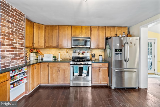 kitchen featuring dark wood-type flooring, appliances with stainless steel finishes, decorative backsplash, and dark stone counters