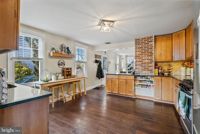 kitchen featuring dark hardwood / wood-style floors, decorative backsplash, stainless steel range with gas stovetop, and kitchen peninsula