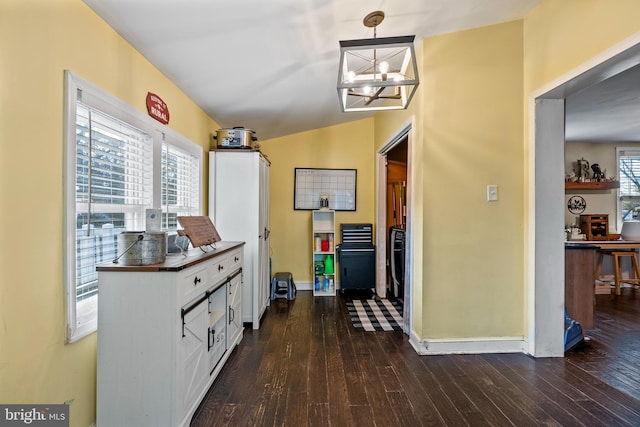 hallway with a healthy amount of sunlight, dark hardwood / wood-style flooring, and a chandelier