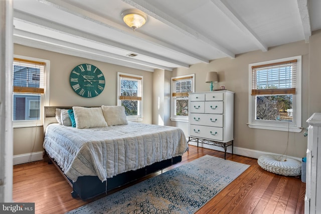 bedroom featuring multiple windows, hardwood / wood-style floors, and beamed ceiling