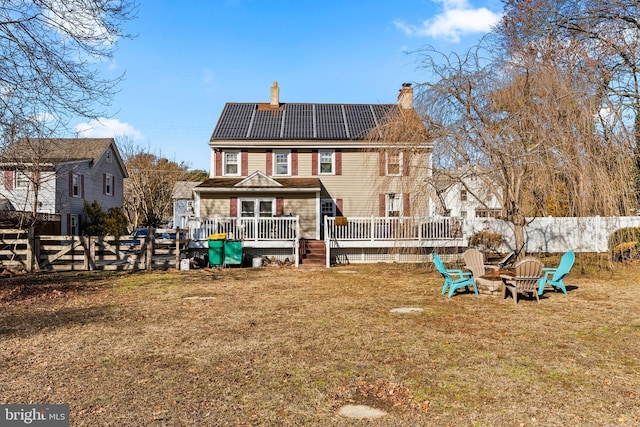 back of house featuring solar panels, a wooden deck, a lawn, and an outdoor fire pit