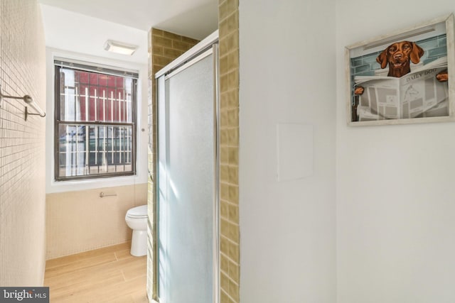 bathroom with hardwood / wood-style flooring, a shower with door, and toilet