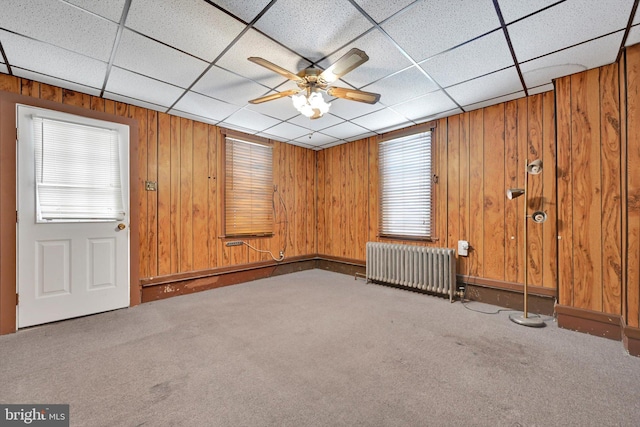 empty room with ceiling fan, radiator heating unit, carpet, and wood walls