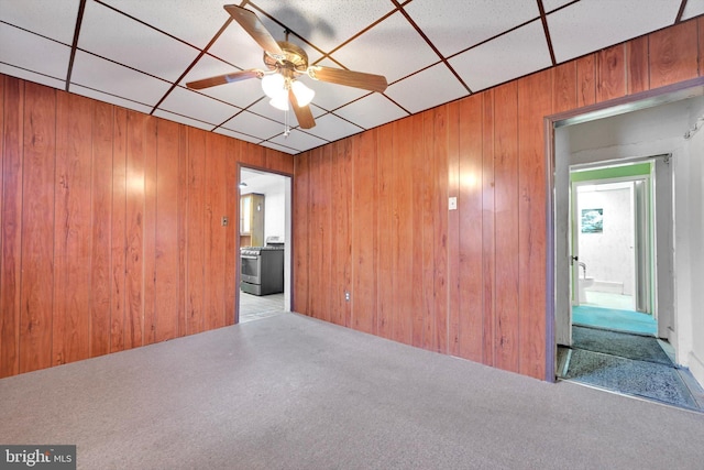 carpeted spare room featuring a drop ceiling, ceiling fan, and wood walls