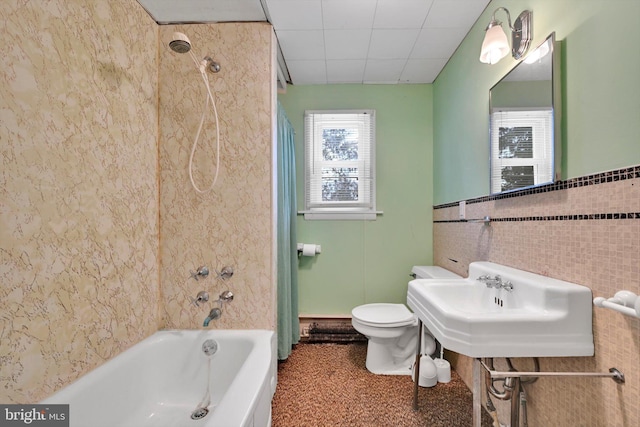 full bathroom with toilet, tiled shower / bath combo, sink, and tile walls