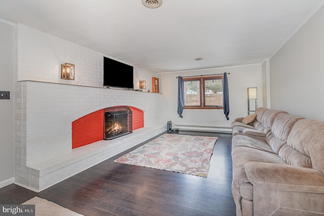 living room featuring dark wood-type flooring, crown molding, a brick fireplace, and a baseboard heating unit