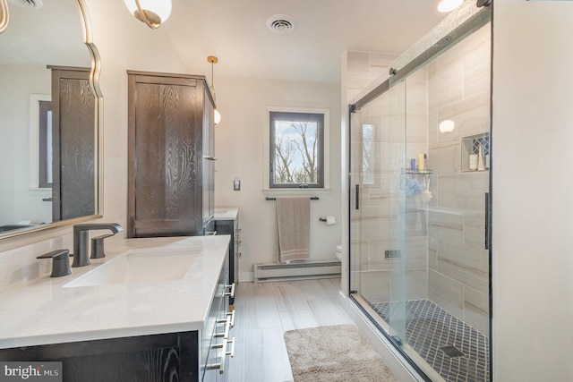 bathroom with a shower with door, vanity, baseboard heating, and toilet