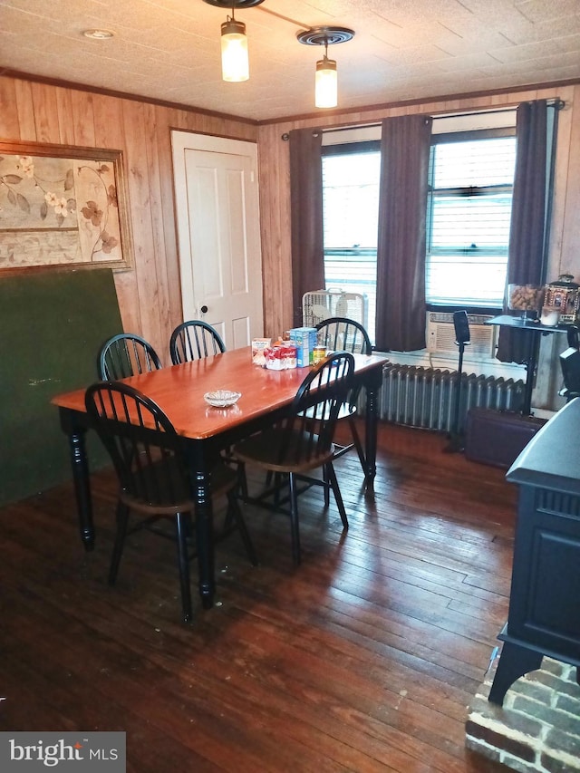 dining space featuring dark wood-type flooring, radiator, and wood walls