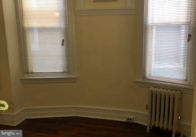 empty room featuring dark wood-type flooring and radiator heating unit