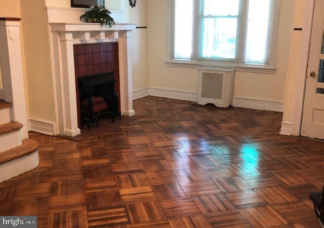 unfurnished living room featuring a tiled fireplace, radiator, and dark parquet flooring