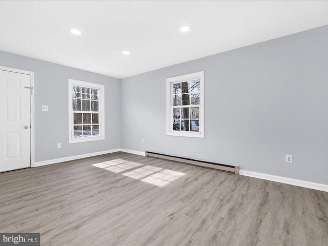 empty room featuring a baseboard heating unit, a wealth of natural light, and light hardwood / wood-style flooring