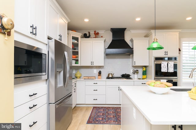 kitchen featuring premium range hood, appliances with stainless steel finishes, pendant lighting, white cabinetry, and sink