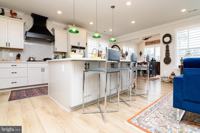 kitchen with a kitchen island with sink, white cabinets, and premium range hood