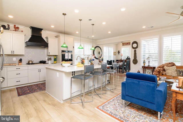 kitchen featuring a kitchen island with sink, decorative light fixtures, white cabinetry, and premium range hood