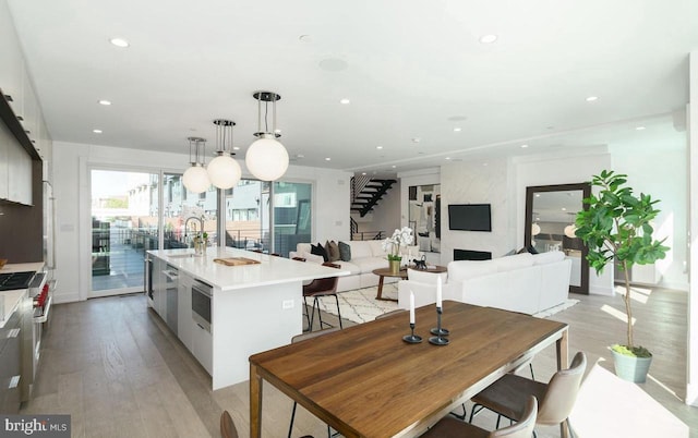 kitchen featuring an island with sink, sink, pendant lighting, and light wood-type flooring