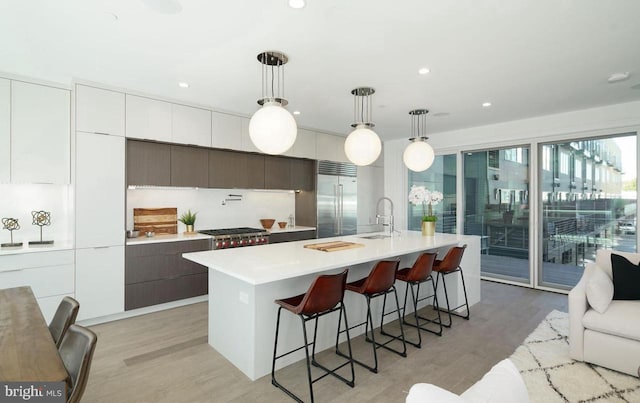 kitchen with built in fridge, decorative light fixtures, sink, a kitchen island with sink, and dark brown cabinets