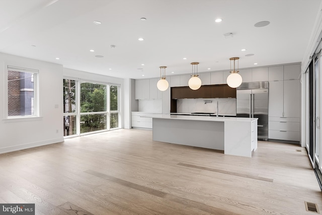 kitchen featuring built in fridge, hanging light fixtures, a center island with sink, and light hardwood / wood-style floors