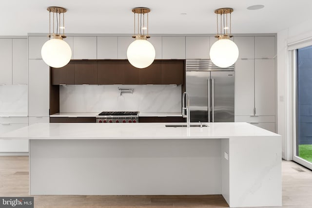 kitchen featuring hanging light fixtures, sink, an island with sink, and stainless steel built in refrigerator