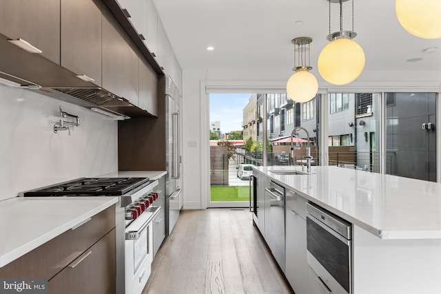 kitchen with sink, light hardwood / wood-style flooring, a kitchen island with sink, hanging light fixtures, and premium appliances