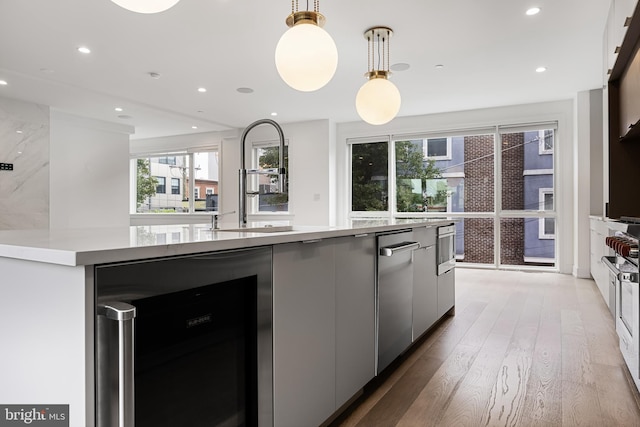 kitchen featuring wine cooler, white cabinetry, hardwood / wood-style flooring, an island with sink, and pendant lighting