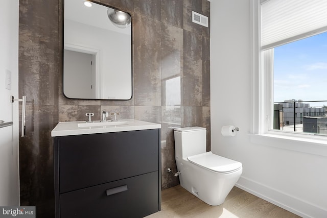 bathroom with vanity, toilet, hardwood / wood-style floors, and tile walls