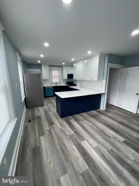 kitchen featuring white cabinetry, stainless steel fridge, a kitchen bar, kitchen peninsula, and dark wood-type flooring