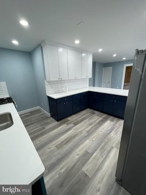 kitchen with sink, white cabinetry, light hardwood / wood-style flooring, stainless steel fridge, and decorative backsplash