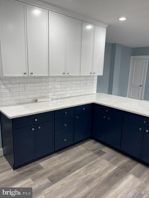 kitchen with blue cabinetry, white cabinets, backsplash, and light hardwood / wood-style flooring