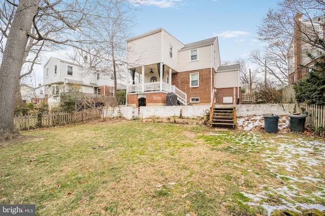 rear view of house with stairs, brick siding, a lawn, and fence