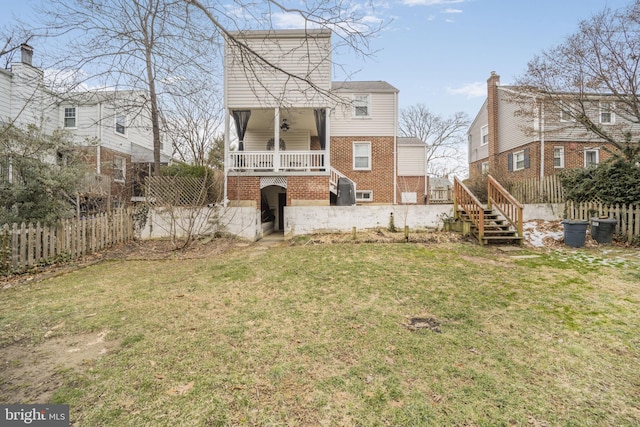 rear view of house with brick siding, covered porch, a lawn, fence private yard, and stairs