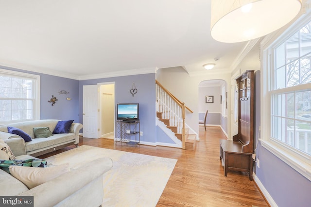 living area featuring arched walkways, baseboards, light wood-style floors, ornamental molding, and stairway