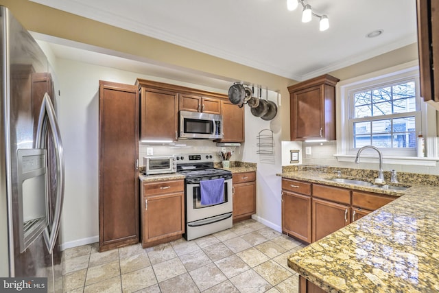 kitchen with brown cabinetry, appliances with stainless steel finishes, ornamental molding, a sink, and backsplash