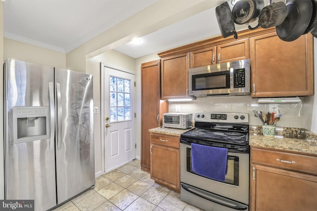 kitchen with brown cabinetry, light stone counters, stainless steel appliances, and decorative backsplash