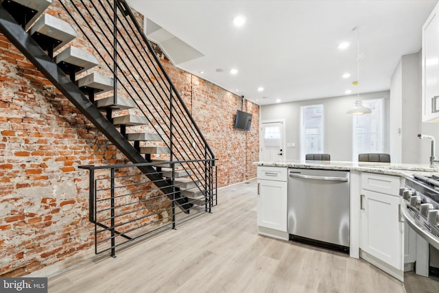 kitchen with white cabinetry, brick wall, stainless steel appliances, and light stone counters