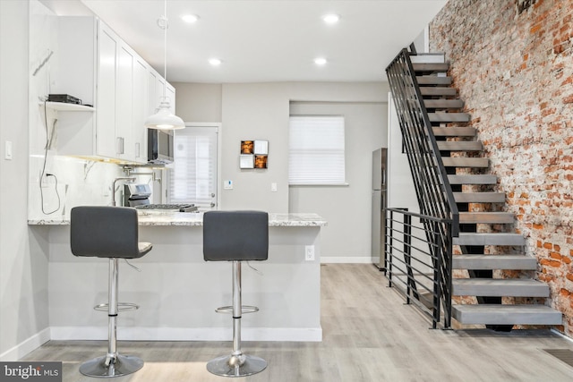 kitchen featuring a kitchen bar, white cabinetry, light hardwood / wood-style flooring, stainless steel refrigerator, and light stone countertops