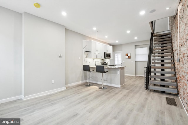 kitchen with white cabinetry, a breakfast bar area, light wood-type flooring, and kitchen peninsula