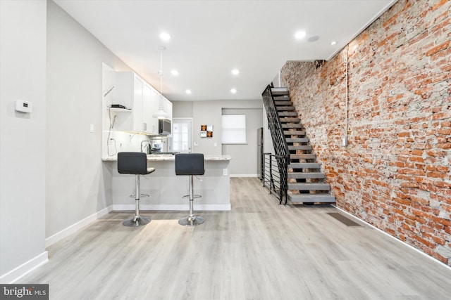 kitchen with a breakfast bar, white cabinets, brick wall, kitchen peninsula, and light wood-type flooring