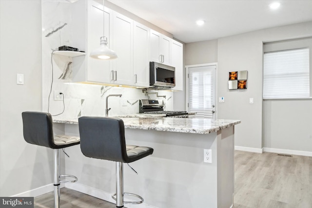 kitchen featuring range, a breakfast bar, kitchen peninsula, and white cabinets