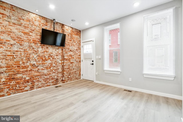 spare room with light hardwood / wood-style floors, a healthy amount of sunlight, and brick wall