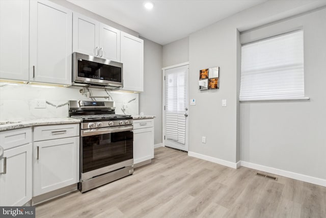 kitchen with light stone countertops, stainless steel appliances, white cabinets, and light wood-type flooring