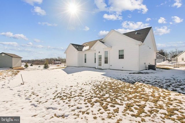 snow covered house with central AC unit and a shed