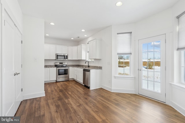 kitchen with sink, white cabinetry, stainless steel appliances, light stone countertops, and dark hardwood / wood-style flooring