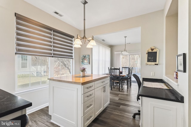 kitchen featuring pendant lighting, butcher block countertops, white cabinets, dark hardwood / wood-style flooring, and a center island