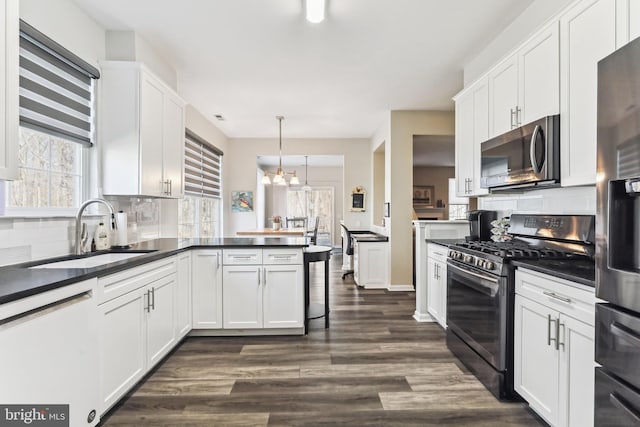 kitchen with pendant lighting, sink, appliances with stainless steel finishes, white cabinets, and kitchen peninsula